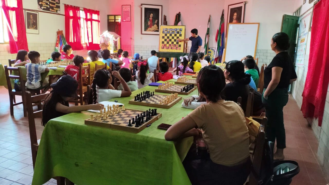 Clase de P.E.C.U. en el colegio Virgen de Urkupiña: un aula llena de alumnos jugando sobre las mesas, con el tablero mural al frente